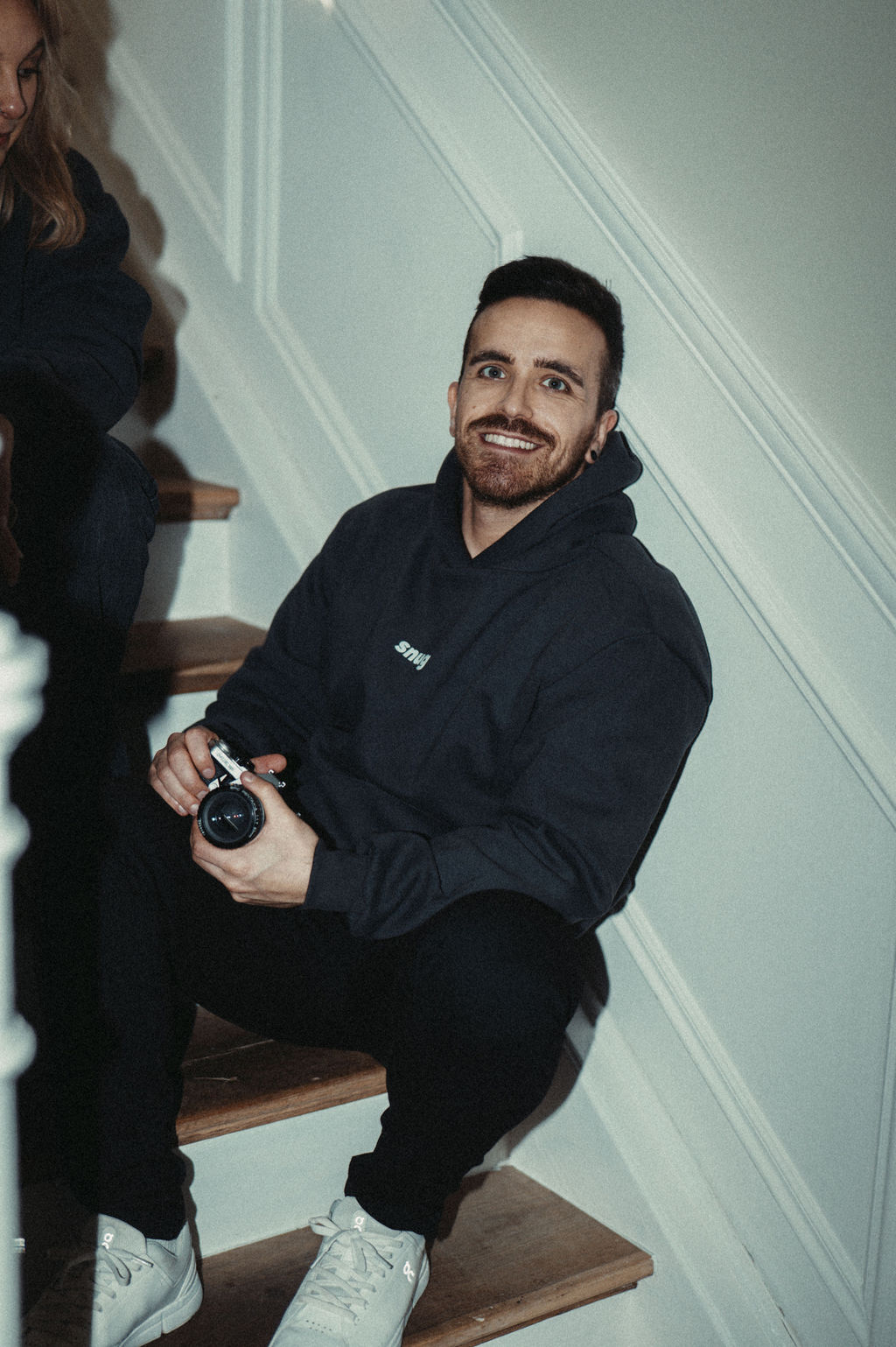 Ricardo sitting on a staircase with a film camera, relaxed and smiling.